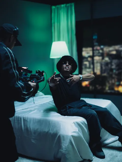 Un camarógrafo graba a Myke Towers sentado en la cama